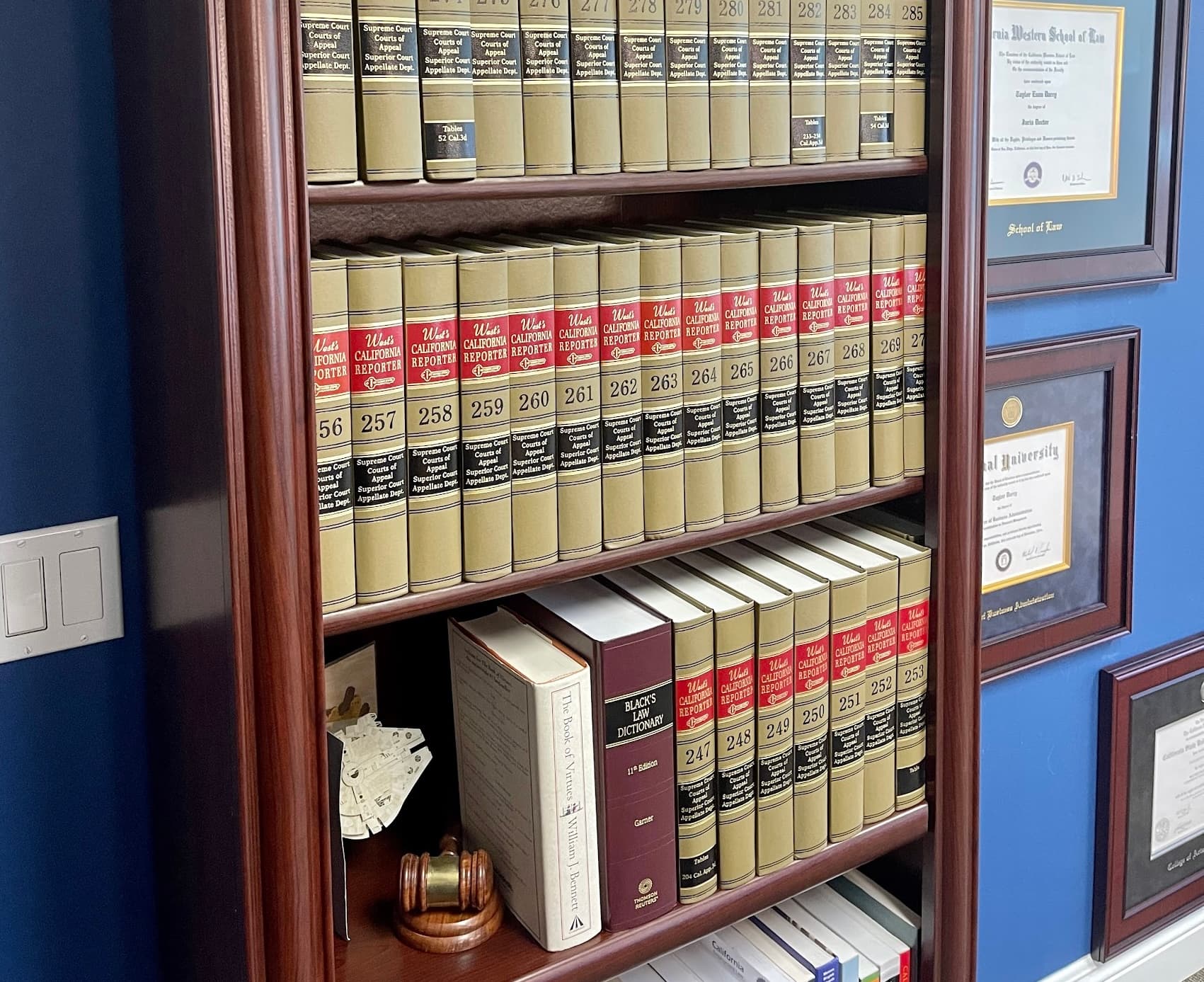 The attorney's working office at Think Legal, P.C., with West's California Reporter volumes, framed law-school diplomas, and a navy accent wall